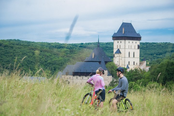 Experience a delightful bike ride to Karlstejn Castle surrounded by lush green hills and scenic rivers as you journey through charming villages and remarkable landscapes of Czechia.